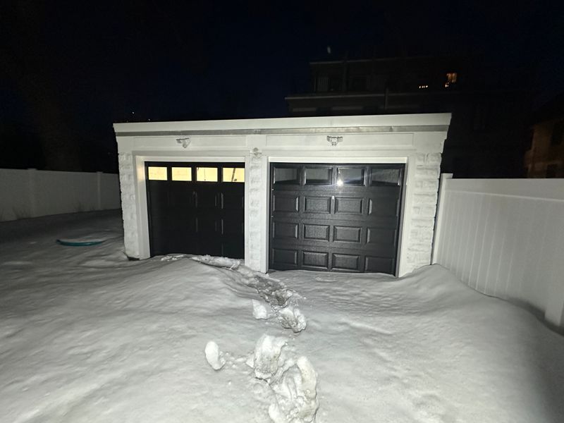 Black dual garage doors with windows on detached garage at night in deep snow
